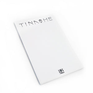 Image of a white notebook against a white background. The top of the notebook says "tinashe" in a black spotted font. The bottom center of the notebook features a black 333 logo. The logo is a 3 facing the right way, mirrored by a 3 facing the opposite way, connected to a large 3 that is sideways and across the bottom of the other two 3's, forming a square shaped logo.
