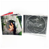 Image of an opened cd case booklet displaying the front cover and the inside of the cd case against a white background. The album artwork is for tinashe's album 333. Tinashe sits inside of a grey circle with green streaks. she has long dark hair and a third eye in the center of her forehead. the top left features the grey 333 logo. The inside of the cd case is white and grey with abstract imaging.