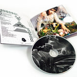 Image of a cd booklet and cd against a white background. The cd and booklet are for tinashe's album "333". the cd is grey and white with abstract imagery. the booklet shows the lyrics to a song in black and white text on the left. The right is an image of tinashe sitting down in a colorful field.