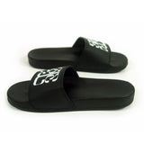 Image of black slide sandals against a white background. The middle of the strap on the slides feature the tinashe 333 logo in white. The logo is a 3 facing the right way, mirrored by a 3 facing the opposite way, connected to a large 3 that is sideways and across the bottom of the other two 3's, forming a square shaped logo. The sandals are facing opposite directions from each other.