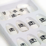 close up Image of white fake nail stickers against a white background. The nails all feature the Tinashe 333 logo on the center of them in black. The logo is a 3 facing the right way, mirrored by a 3 facing the opposite way, connected to a large 3 that is sideways and across the bottom of the other two 3's, forming a square shaped logo.