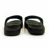 Image of black slide sandals against a white background. The middle of the strap on the slides feature the tinashe 333 logo in white. The logo is a 3 facing the right way, mirrored by a 3 facing the opposite way, connected to a large 3 that is sideways and across the bottom of the other two 3's, forming a square shaped logo. The logo is not visible in this image as the sandals are photographed from the back.