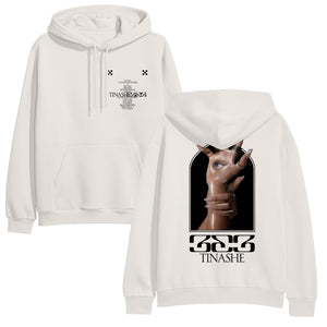 Image of the front and back of a bone colored hoodie against a white background. The left chest features two small black checkerboard designs. Below in black is the track listing to tinashe's album "333". over top of the words in black text reads "tinashe 333". The back of the hoodie features an image of a hand with long nails and an eye in the center of the palm. Another hand with long nails grips around the wrist of the hand with the eye. Below this in black says "333" and below that in says "tinashe".