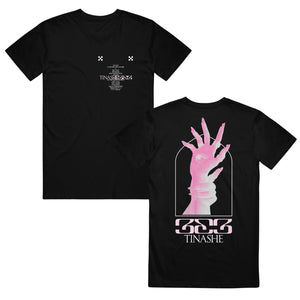 Image of the front and back of a black tshirt against a white background. The left chest features two small white checkerboard designs. Below in white is the track listing to tinashe's album "333". over top of the words in light pink text reads "tinashe 333". The back of the tee features a graphic of a light pink and white hand with an eye in the center of the palm. Another hand grips around the wrist of the hand with the eye. Below this in pink text says "333" and below that in white says "tinashe".