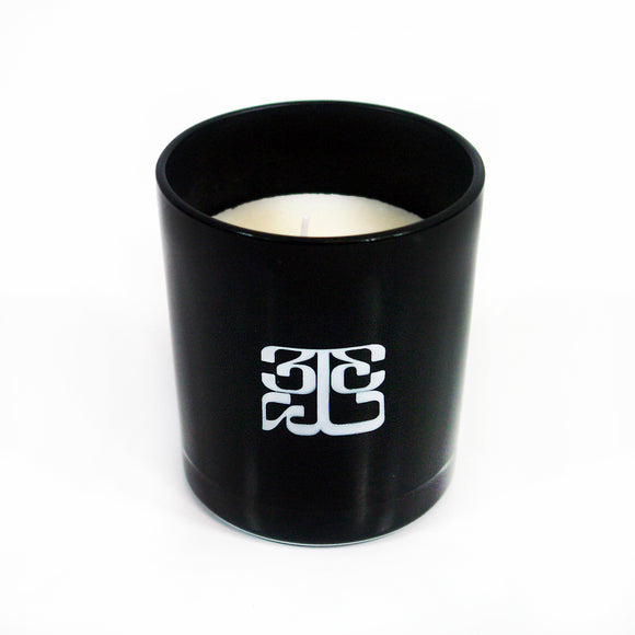 Image of a black candle against a white background. The cylindrical candle holder is black with a white 333 logo on it. The logo is a 3 facing the right way, mirrored by a 3 facing the opposite way, connected to a large 3 that is sideways and across the bottom of the other two 3's, forming a square shaped logo. the candle inside is white.